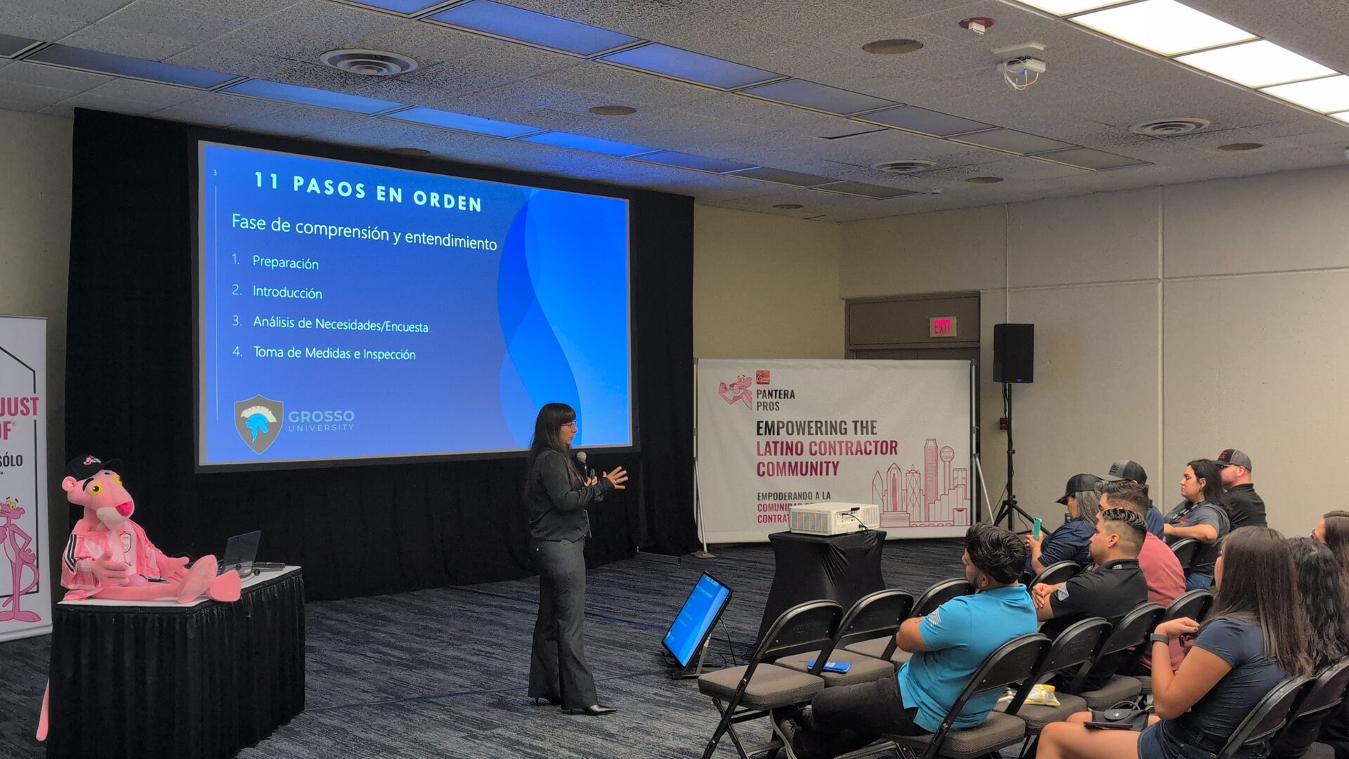 Wendy Harmeyer presenting a Spanish-language Grosso University slide titled "11 Pasos en Orden" to a seated audience.