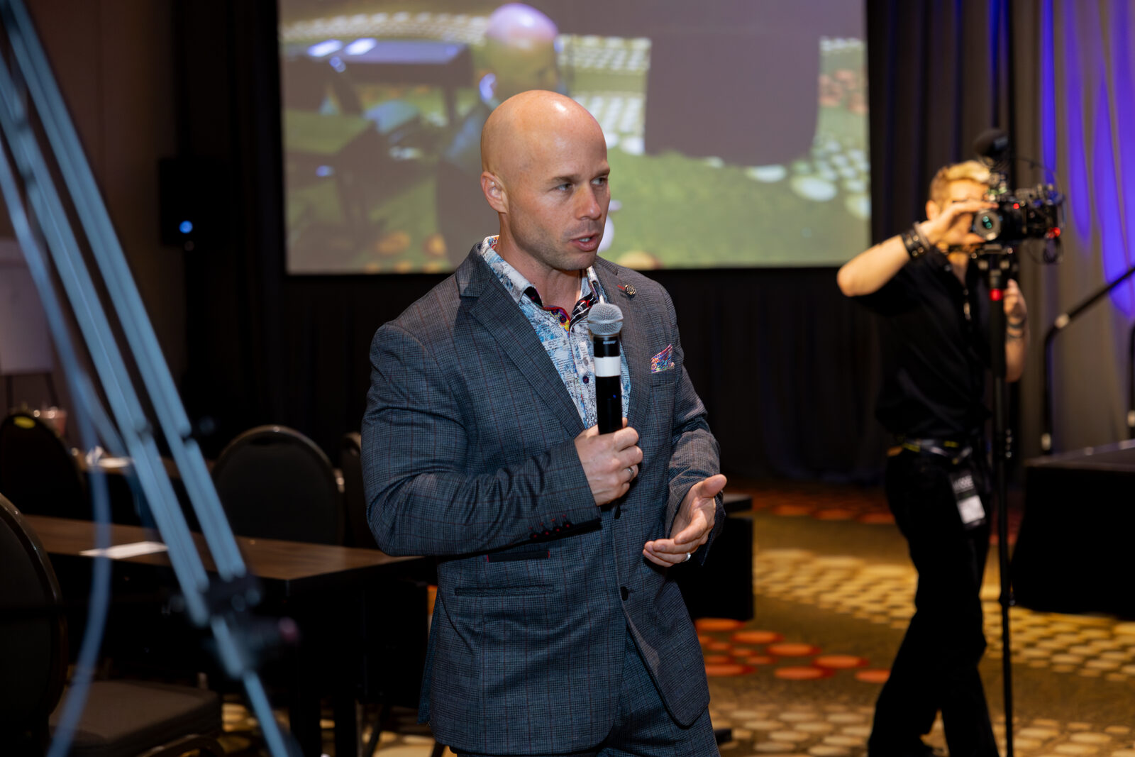 Dominic Caminata speaking into a microphone during an AGOGE 2024 breakout session while a camera operator films him from behind.