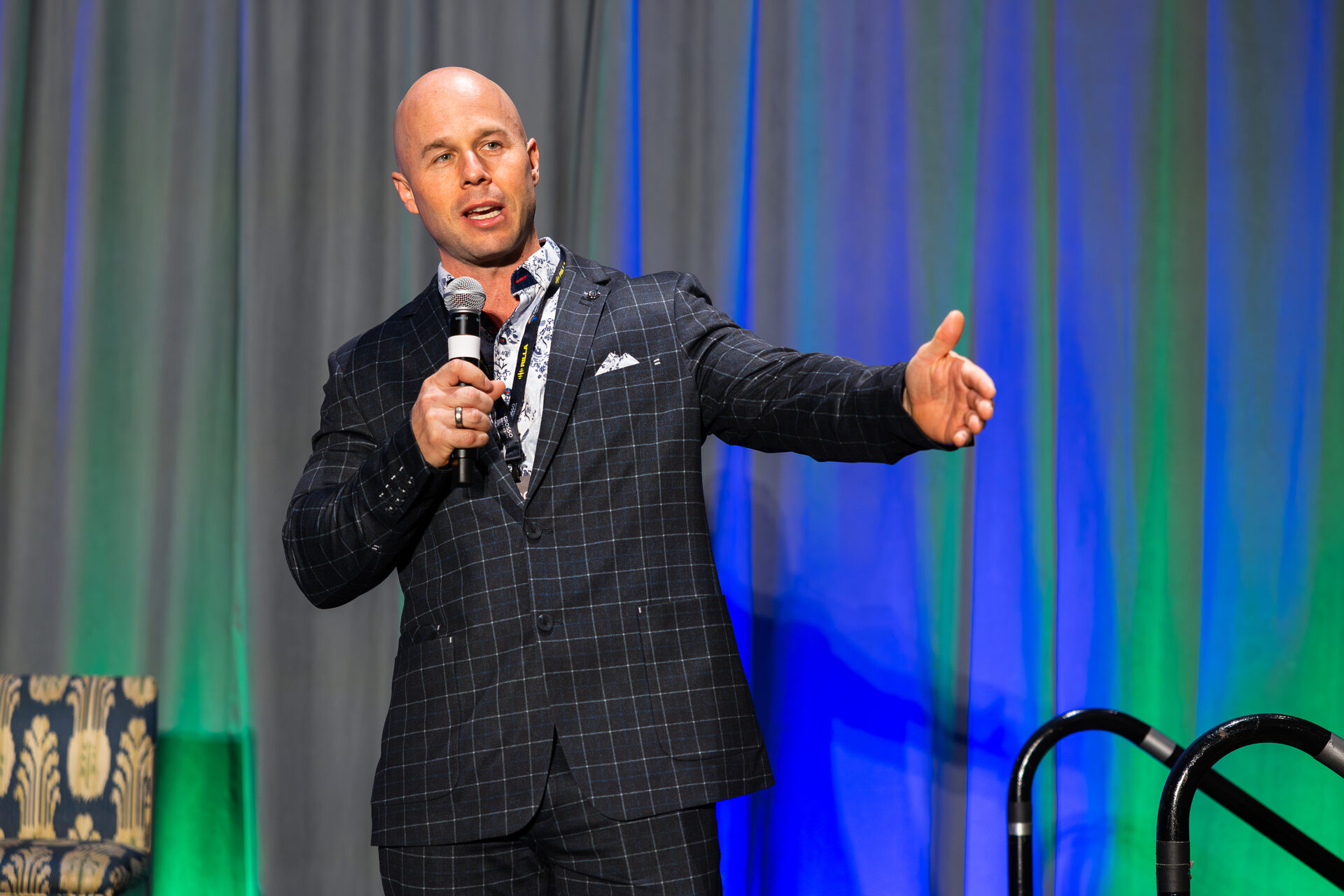 Dominic Caminata mid-sentence on stage at AGOGE 2024, holding a microphone with his free arm extended toward the audience.
