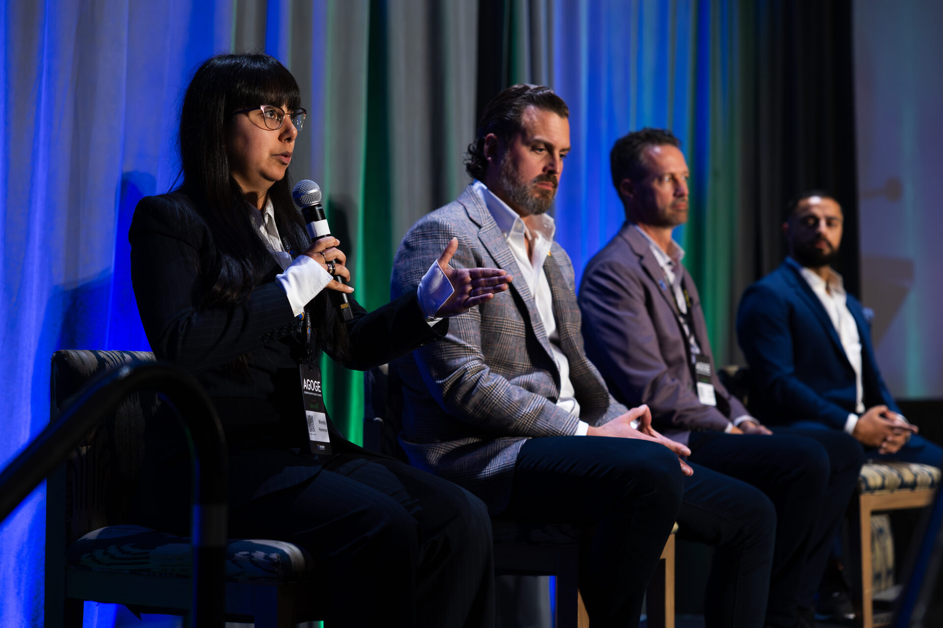 A four-person panel at AGOGE 2024 seated on stage stools; Wendy Harmeyer speaks into a microphone while three other panelists listen.