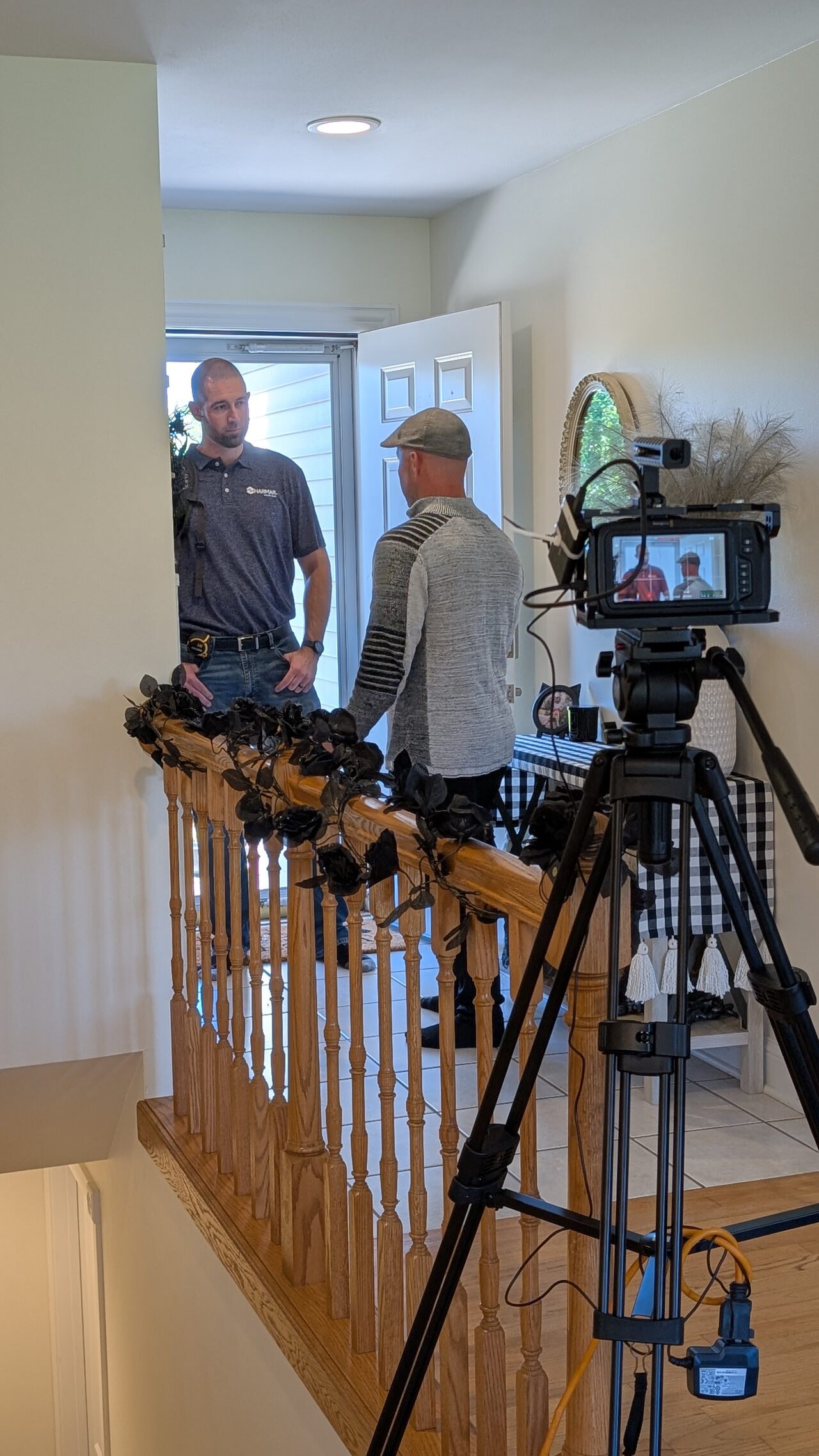 A camera on a tripod films a sales representative being greeted at a homeowner's front door.