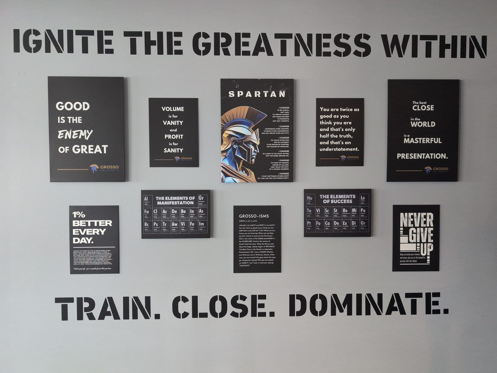 A gray office wall stenciled "Ignite the greatness within" above and "Train. Close. Dominate." below, framing nine black Grosso University principle posters.
