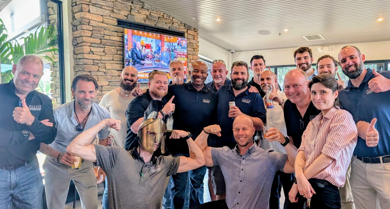 A large group of attendees and staff crowded together for a photograph in a restaurant, several giving a thumbs up.